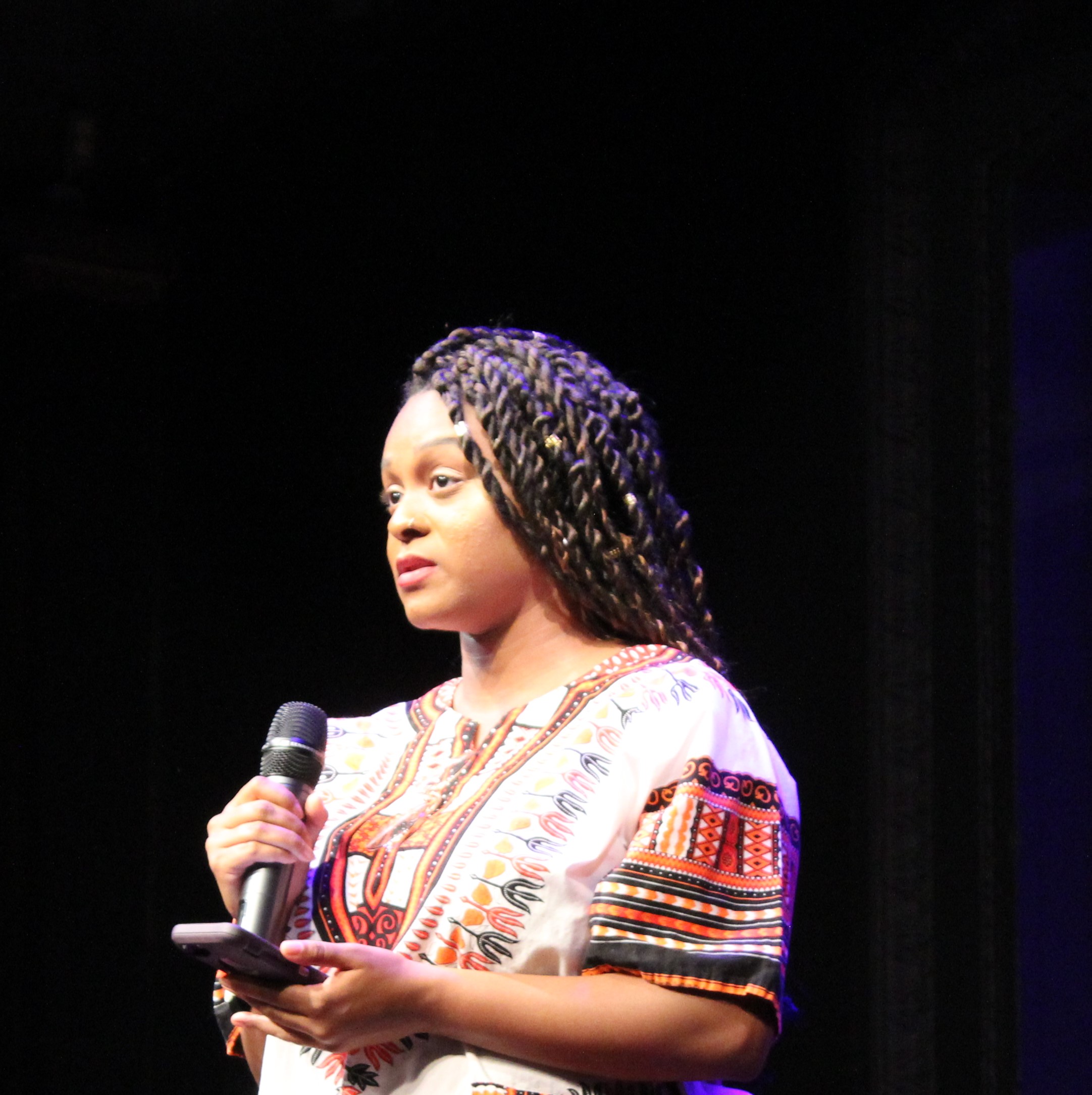 Black Woman with long braids in dashiki in spotlight on darkened stage